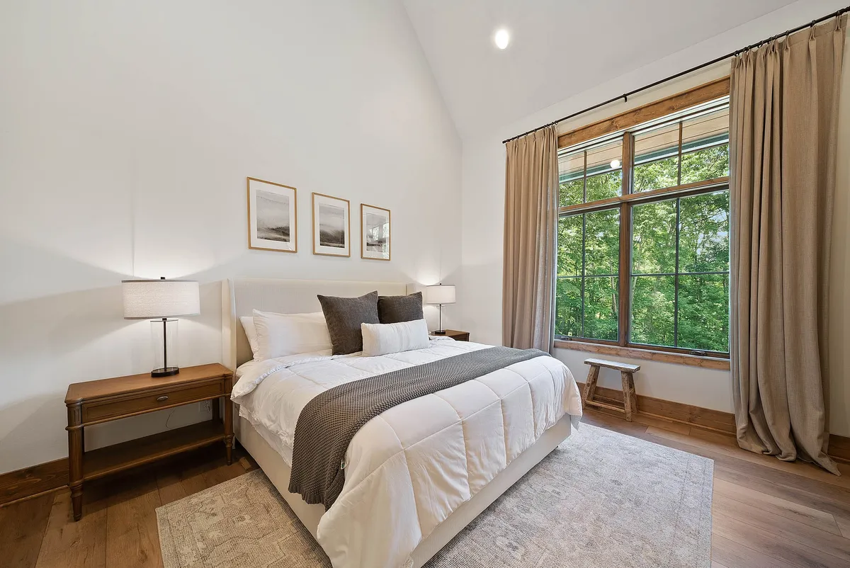 A serene bedroom featuring a comfortable bed flanked by nightstands, a large window letting in abundant natural light, and framed pictures adorning the wall. The soft lighting and uncluttered arrangement foster a sense of privacy and calm.