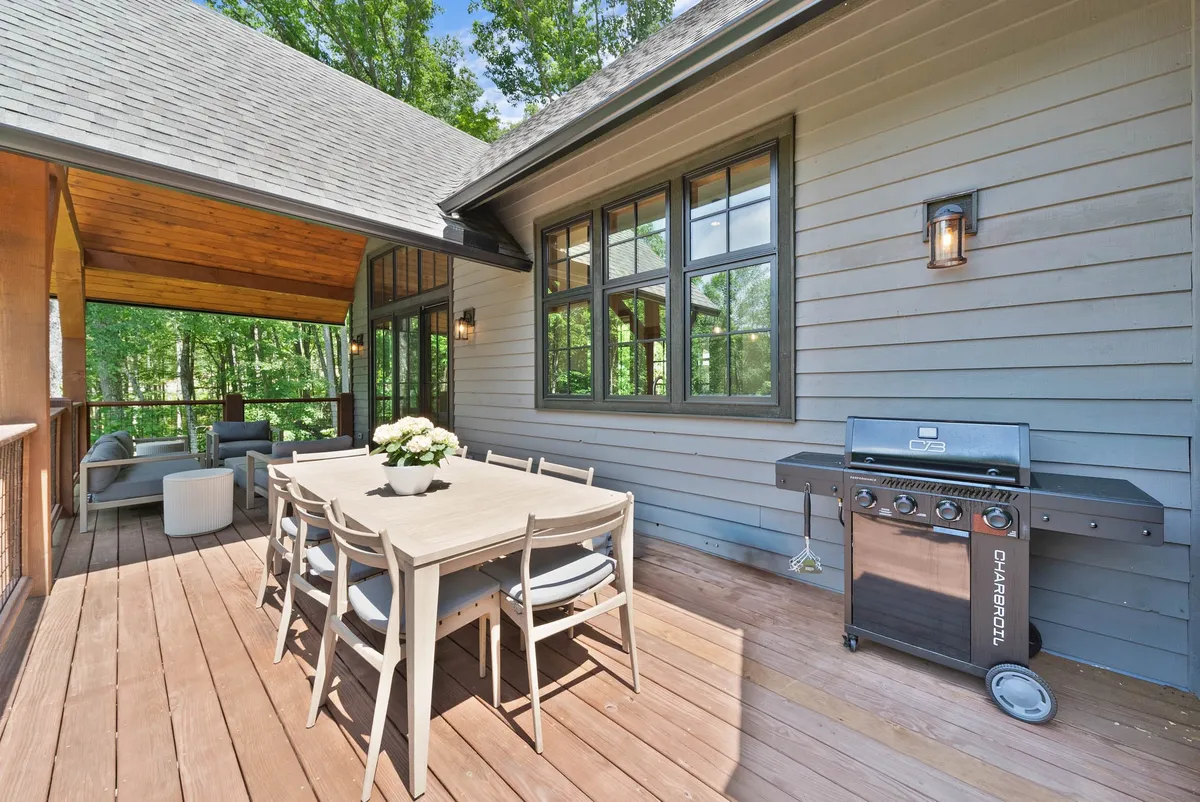 An uncovered outdoor deck featuring a dining table and grill, surrounded by greenery and designed for social gatherings, barbecues, and celebrations. The open-air layout emphasizes unrestricted enjoyment of the outdoors.
