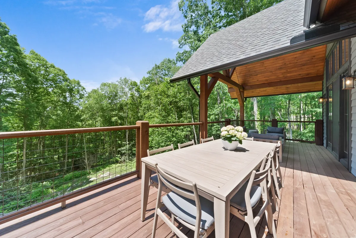 A covered porch with a dining table set amidst lush greenery, offering a peaceful space for enjoying meals outdoors. The setting is tranquil, with natural views and comfortable seating for groups or families.
